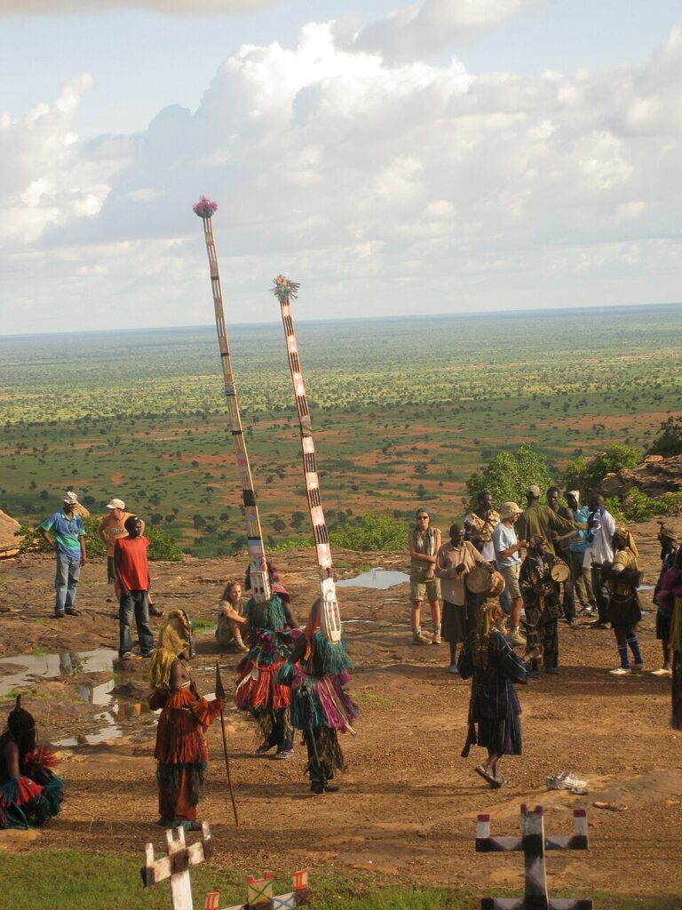 Dogon mask dance with tall headdresses performed on the Sahel plains near the cliff